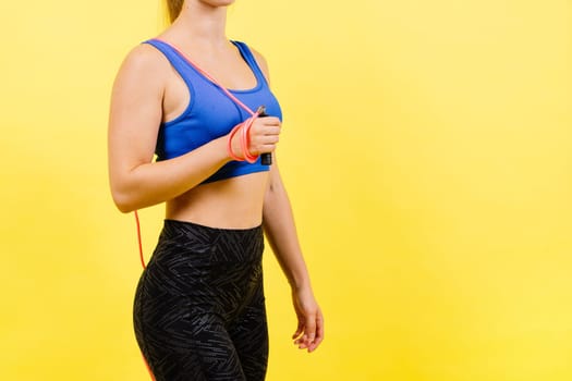 Portrait of gentle muscular woman holding skipping rope on her neck over yellow background