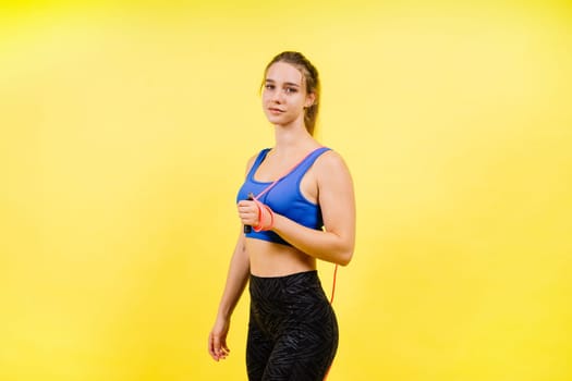 Portrait of gentle muscular woman holding skipping rope on her neck over yellow background