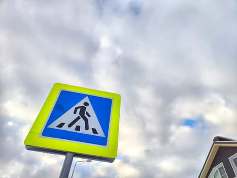 A pedestrian crossing sign on the background of a gray sky with clouds. Drawing, pictogram for pedestrians crossing the road