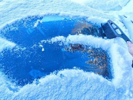 Winter Morning Car Snow Clearing. Person brushing snow off car on frosty winter morning. Difficulties in travel and trip in cold months