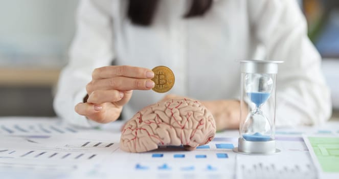 Business woman holding bitcoin coin in front of brain mockup and hourglass closeup. When to buy cryptocurrency concept