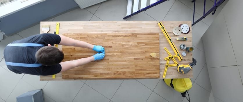 Top view of construction worker polishing wood. Male in protective gloves. Tools and sander machine on other side of table. Renovation and carpenter job concept