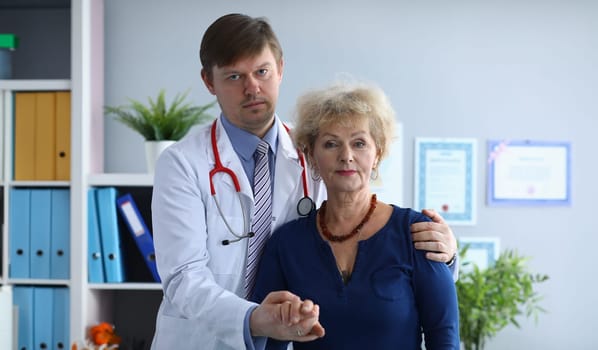 Male doctor in clinic hugs an elderly sad patient. Family doctor helps an elderly woman cope with fear coronavirus infection. Patient is discussing self-isolation with doctor. Social isolation elderly