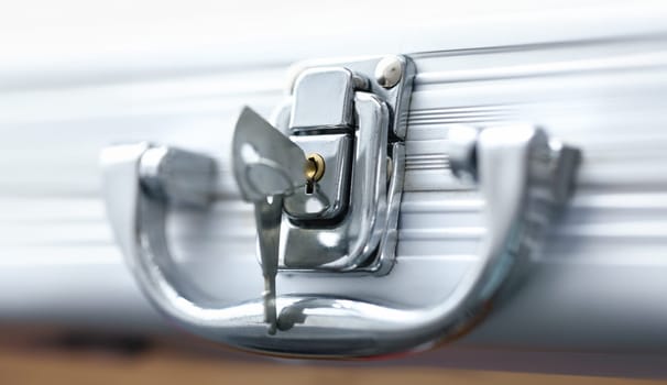 Close-up view of keys inserted in keyhole of aluminum briefcase. Macro shot of closed case. Rectangular container keeps important papers or money. Security and safety concept