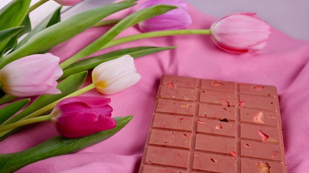 A bar of pink ruby chocolate with sublimated freeze-dried strawberries and almonds and spring tulip flowers . A dessert based on berries and nuts for International Women's Day, March 8, mother's day