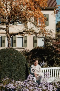 a girl sits on a bench in the park and enjoys the sun. Portrait young adult attractive woman enjoy sitting on bench and relaxing calm carefree rest in city park against green grass and trees on sunny day. Single female person relaxing chilling outdoors