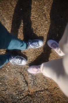 View from above of male and female feet in sports shoes or sneakers, standing on the rocky cliff. POV