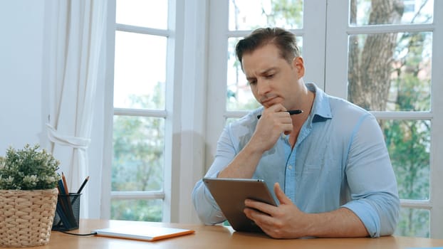 Businessman struggle to solve work problem from home using laptop, sitting on his desk at home office with stressed and frustrated expression, trying to figure out solution for problem. Synchronos