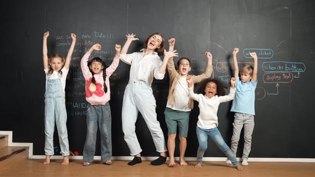 Multicultural happy student and teacher smiling and standing at blackboard with engineering code or prompt written. Kid express feeling of happy and enjoy with studying in STEM classroom. Erudition.