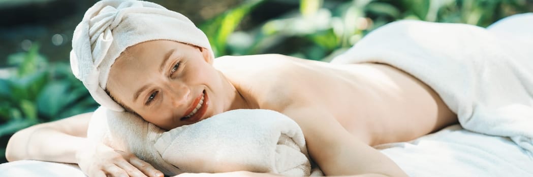Beautiful young woman relaxes on a spa bed surrounded by nature. ready for a body massage. Attractive female in white towel lying peacefully during waiting for body massage. Close up. Tranquility