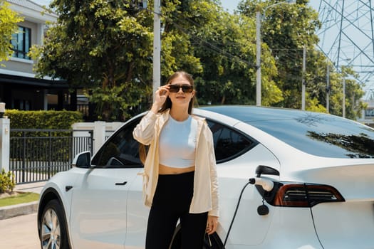 Eco-friendly conscious woman recharging EV vehicle from home charging station. EV electric car technology utilized as alternative transportation for future sustainability. Expedient