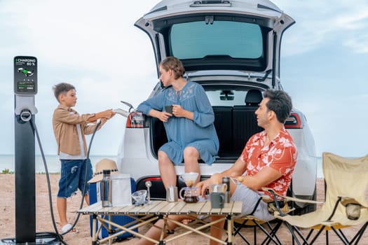 Family vacation trip traveling by the beach with electric car, happy family recharge EV car, enjoying outdoor camping coffee. Seascape travel and eco-friendly car for clean environment. Perpetual