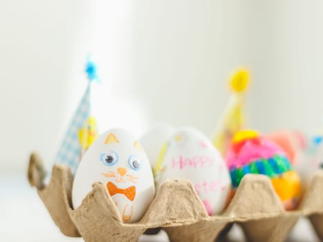 Cardboard package with decorated Easter eggs with glued and painted Easter bunny faces on a marble table with depth of field, side view. The concept of diy, crafts, children art, artisanal, handicraft, diy.