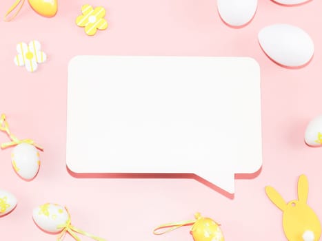 Empty white callout, decorative yellow-white eggs, and a wooden easter bunny lie on a light pink background with copy space for your tex, flat lay close-up. Happy easter concept, holiday banner, blank.