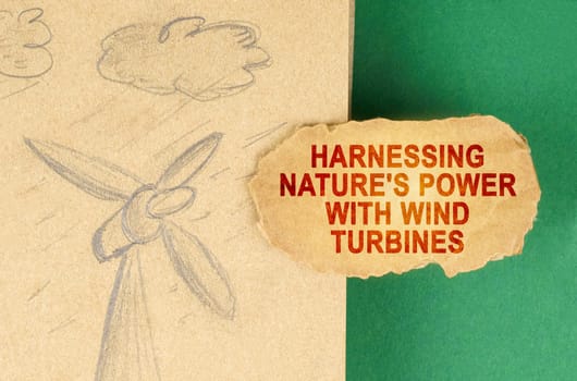 Alternative energy concept. On a green surface there is a drawing with a wind generator and a cardboard with the inscription - Harnessing nature's power with wind turbines