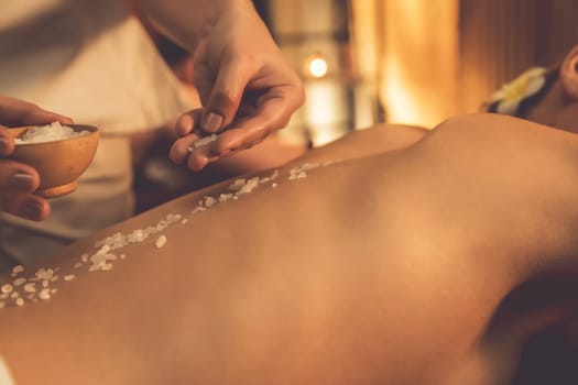 Closeup couple customer having exfoliation treatment in luxury spa salon with warmth candle light ambient. Salt scrub beauty treatment in Health spa body scrub. Quiescent