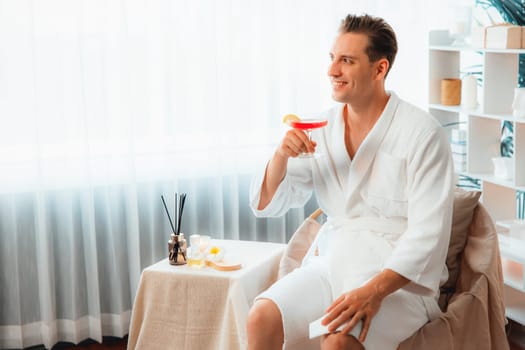 Beauty or body treatment spa salon vacation lifestyle concept with man wearing bathrobe relaxing with drinks in luxurious hotel spa or resort room. Vacation and leisure relaxation. Quiescent