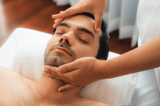 Caucasian man enjoying relaxing anti-stress head massage and pampering facial beauty skin recreation leisure in dayspa modern light ambient at luxury resort or hotel spa salon. Quiescent