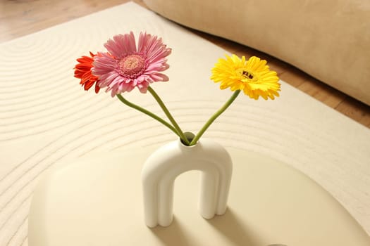 Three colored gerbera flowers in a vase on a table as part of a beige room design. High quality photo