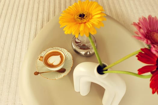 Gerbera flowers and a cup of coffee on a table in a beige bedroom. High quality photo