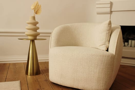 A soft chair and a decorative vase in a beige room on the background of a fireplace. High quality photo
