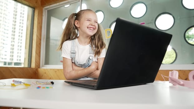 Cute girl using laptop programing software while looking and laughing at camera. Pretty child smiling while crossing arms with funny innocent mood in Stem class. Smart student portrait.Erudition.