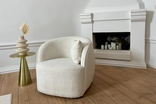 A soft chair and a decorative vase in a beige room on the background of a fireplace. High quality photo