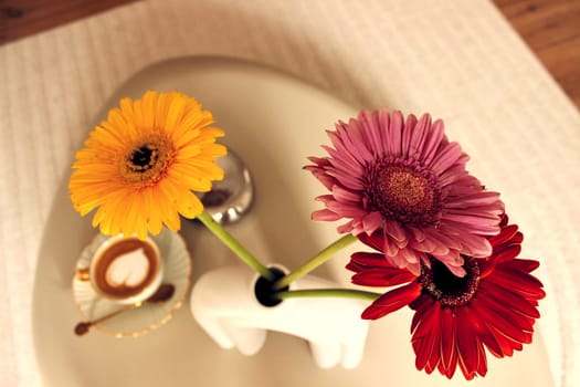 Gerbera flowers and a cup of coffee on a table in a beige bedroom. High quality photo