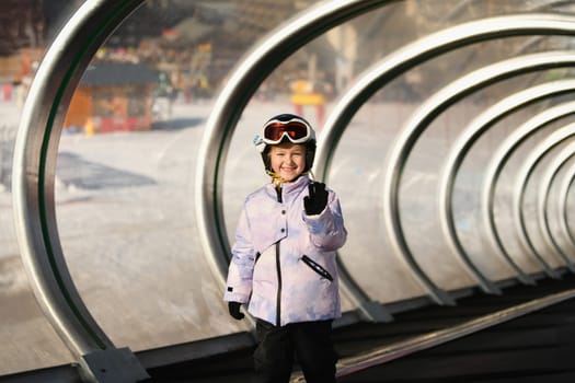 A girl on skis stands on a carpet ski lift in a tunel