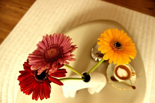 Gerbera flowers and a cup of coffee on a table in a beige bedroom. High quality photo
