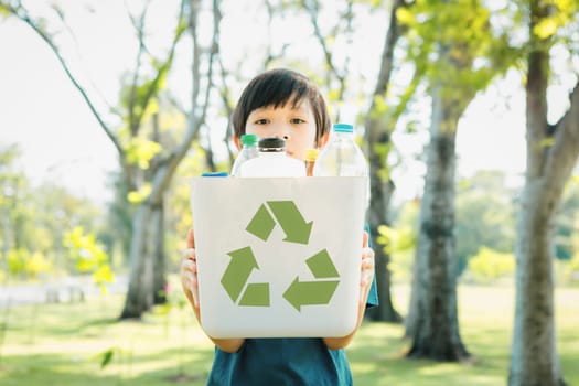 Cheerful young asian boy holding recycle symbol bin on daylight natural green park promoting waste recycle, reduce, and reuse encouragement for eco sustainable awareness for future generation. Gyre