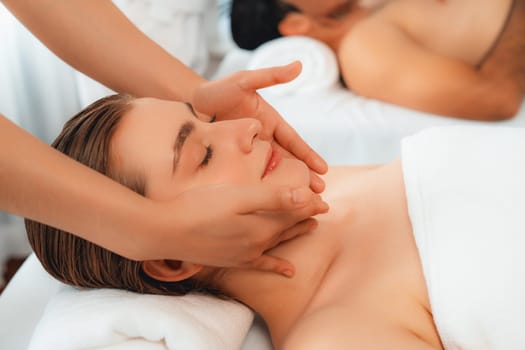 Caucasian couple enjoying relaxing anti-stress head massage and pampering facial beauty skin recreation leisure in dayspa modern light ambient at luxury resort or hotel spa salon. Quiescent