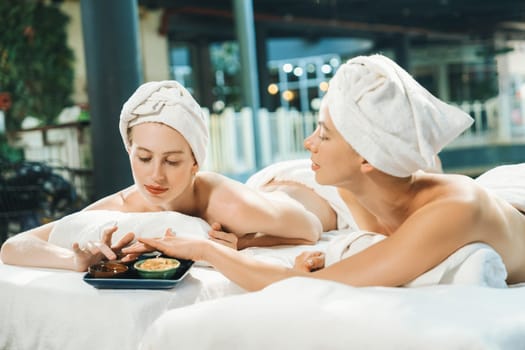 Couple of beautiful young girls lie on spa bed during interested in homemade beauty facial mask. Attractive woman touching herbal facial mask. Surrounded with nature environment. Tranquility.