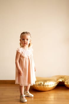 Little girl in a dress stands in a room near an inflatable golden figure. High quality photo