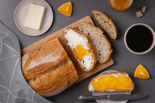 Cup of coffee, sandwich with orange jam, loaf of bread on the grey background. Breakfast concept.