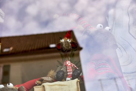 Whimsical New Year's Mouse in Cap and Scarf Stands Behind Store Display. Capture the charm of the holiday season with this delightful image featuring a toy mouse or rat wearing a comical New Year's cap and scarf, playfully standing behind a shop window display. The festive scene adds a touch of whimsy to your creative projects, invoking the spirit of celebration and joy.