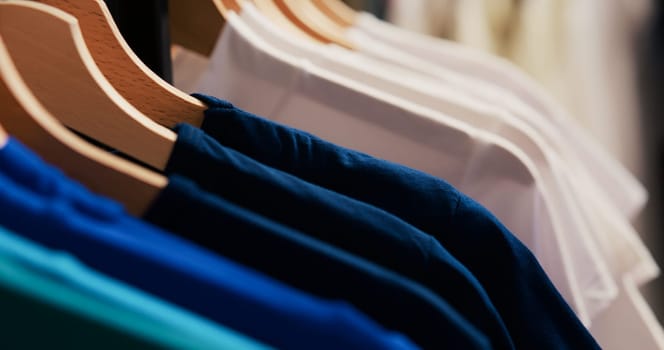 Selective focus of hangers and racks filled with basic shirt, empty modern boutique with fashionable clothes. Shopping centre equipped new fashion collection waiting for customers.