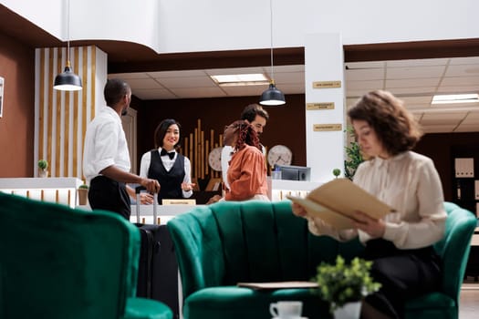 Adult providing good check in experience at luxury hotel, asking guests to see room reservation. Receptionist working at front desk to assist tourists with their booking details in lobby.