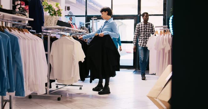 Cheerful employee arranging stylish clothes, working at modern boutique visual. Caucasian manager putting hangers with fashionable merchandise on racks in shopping centre. Fashion concept