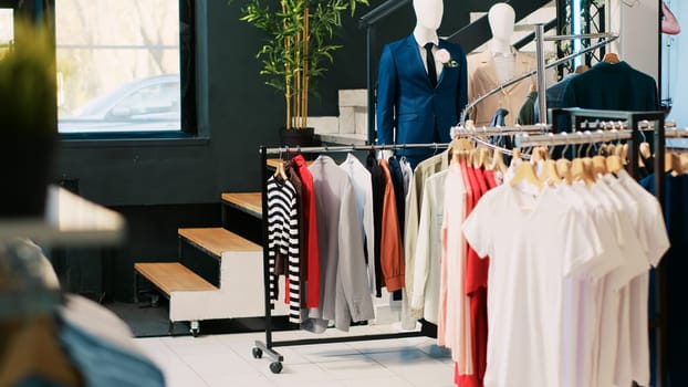 Interior of modern boutique with trendy clothes on racks, fashionable merchandise and formal wear in clothing store. Empty showroom in shopping mall with new fashion collection on hangers