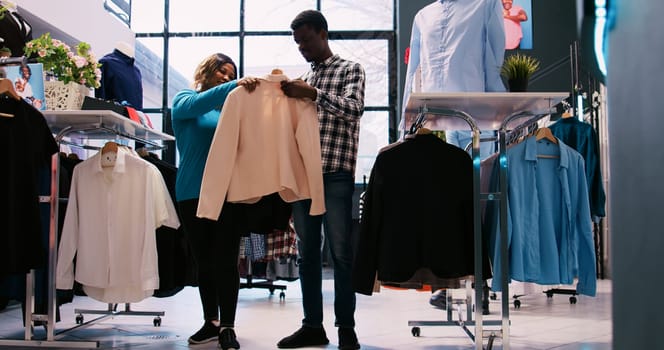 African american clients looking at sale merchandise, buying formal wear in modern boutique. Fashionable couple checking stylish outfit material in shopping centre. Fashion concept