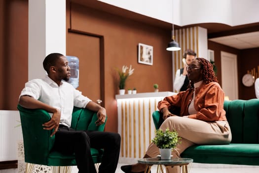 Tourists with booking reservation at hotel, sitting in lounge area and talking about new holiday plan. Young couple waiting to do check in and register at front desk, luxury resort.