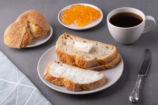 Sandwiches with butter, a cup of coffee and apricot jam on a gray background. Breakfast concept.