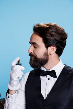 Hotel porter using cologne bottle to smell nice, applying perfume on camera and feeling confident while he wears professional formal suit with tie. Employee spraying fresh aromatic scent. Close up.