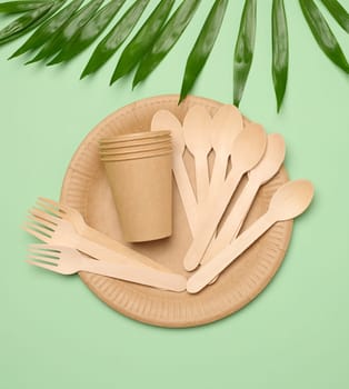 Paper plates and cups, wooden spoons and forks on a green background, top view