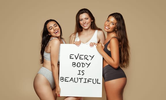 Positive young multiethnic women in different underwear, enjoy natural beauty, hold banner inscription every body is beautiful, isolated on beige background, studio. Lifestyle, health care, love
