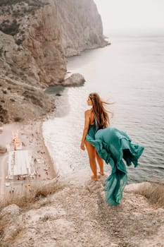 Woman sea trevel green dress. Side view a happy woman with long hair in a long mint dress posing on a beach with calm sea bokeh lights on sunny day. Girl on the nature on blue sky background