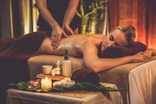 Caucasian woman customer enjoying relaxing anti-stress spa massage and pampering with beauty skin recreation leisure in warm candle lighting ambient salon spa at luxury resort or hotel. Quiescent