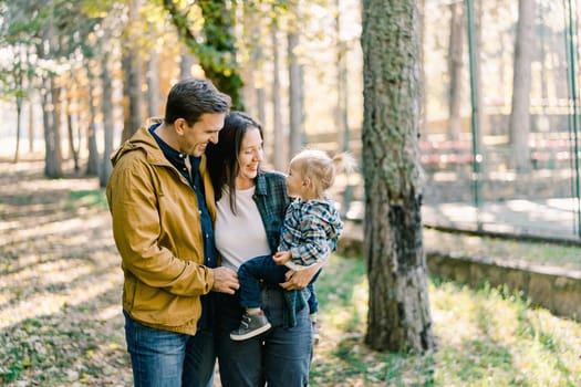 Dad hugs mom with a little girl in her arms while standing in the park. High quality photo