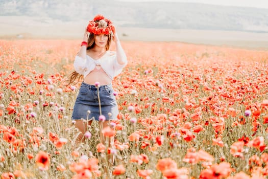 Happy woman in a poppy field in a white shirt and denim skirt with a wreath of poppies on her head posing and enjoying the poppy field